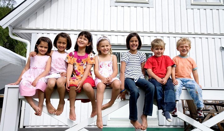 Foto: NTB scanpix Credit: Oslo kommune Gruppe barn sitter på gjerde foran hus.